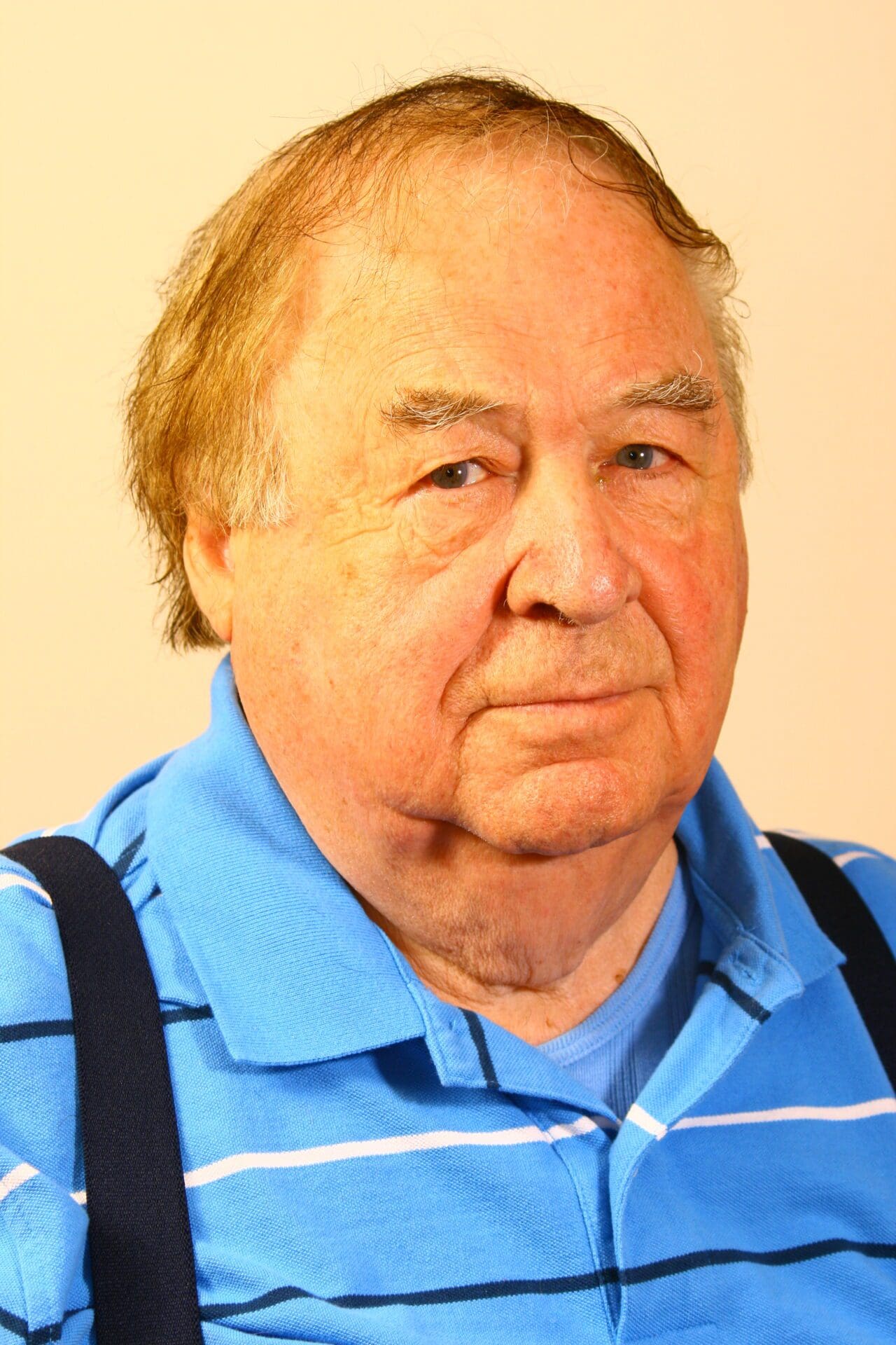 An older man wearing a blue shirt and suspenders.