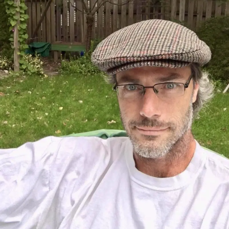 A man wearing glasses and a hat in the yard.