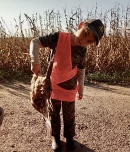 A young boy holding a dead bird in a corn field.