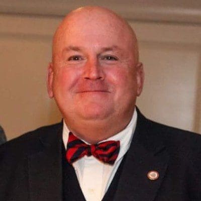 A bald man in a suit and bow tie smiles for the camera.