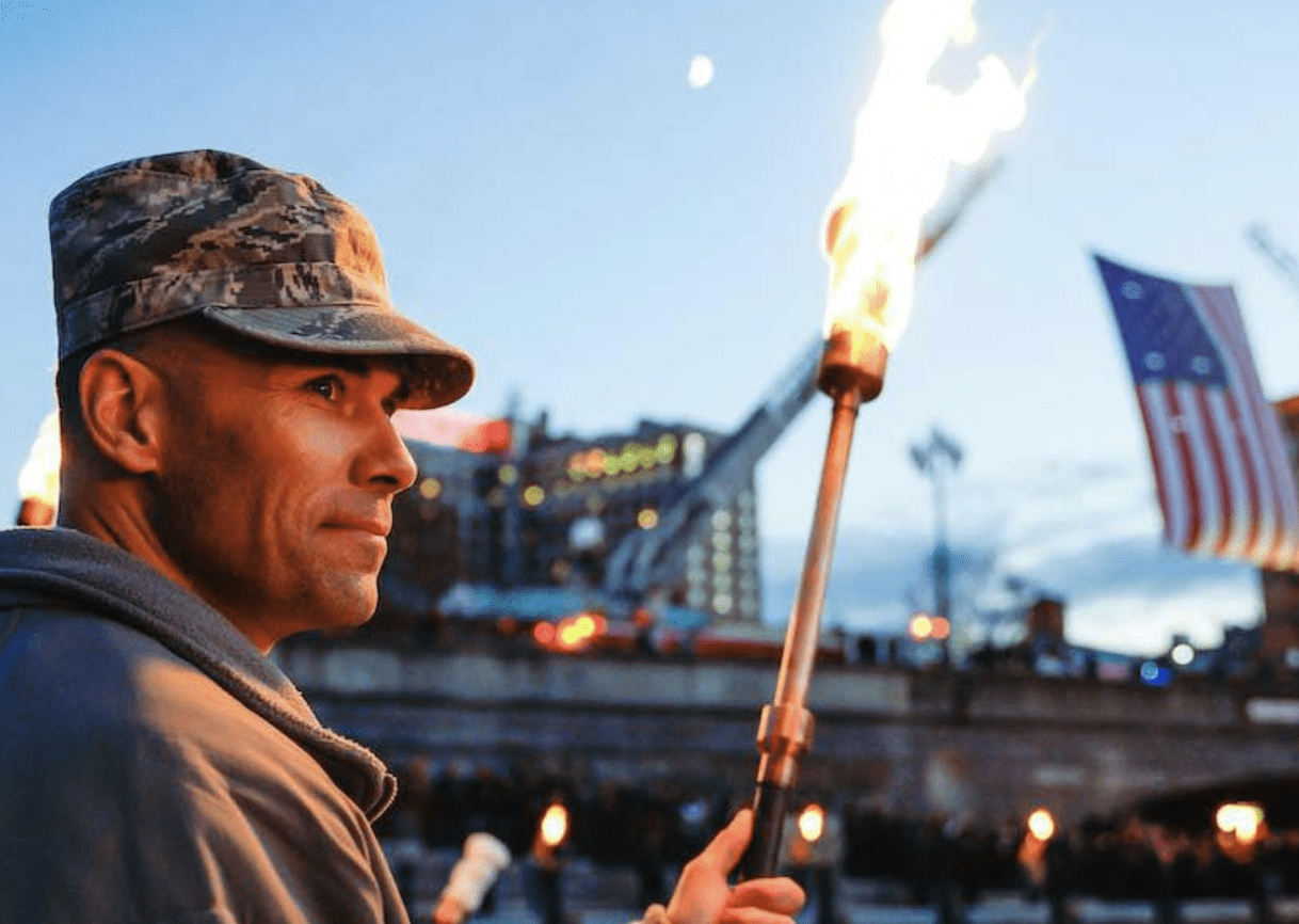 A man holding a torch in front of an american flag.