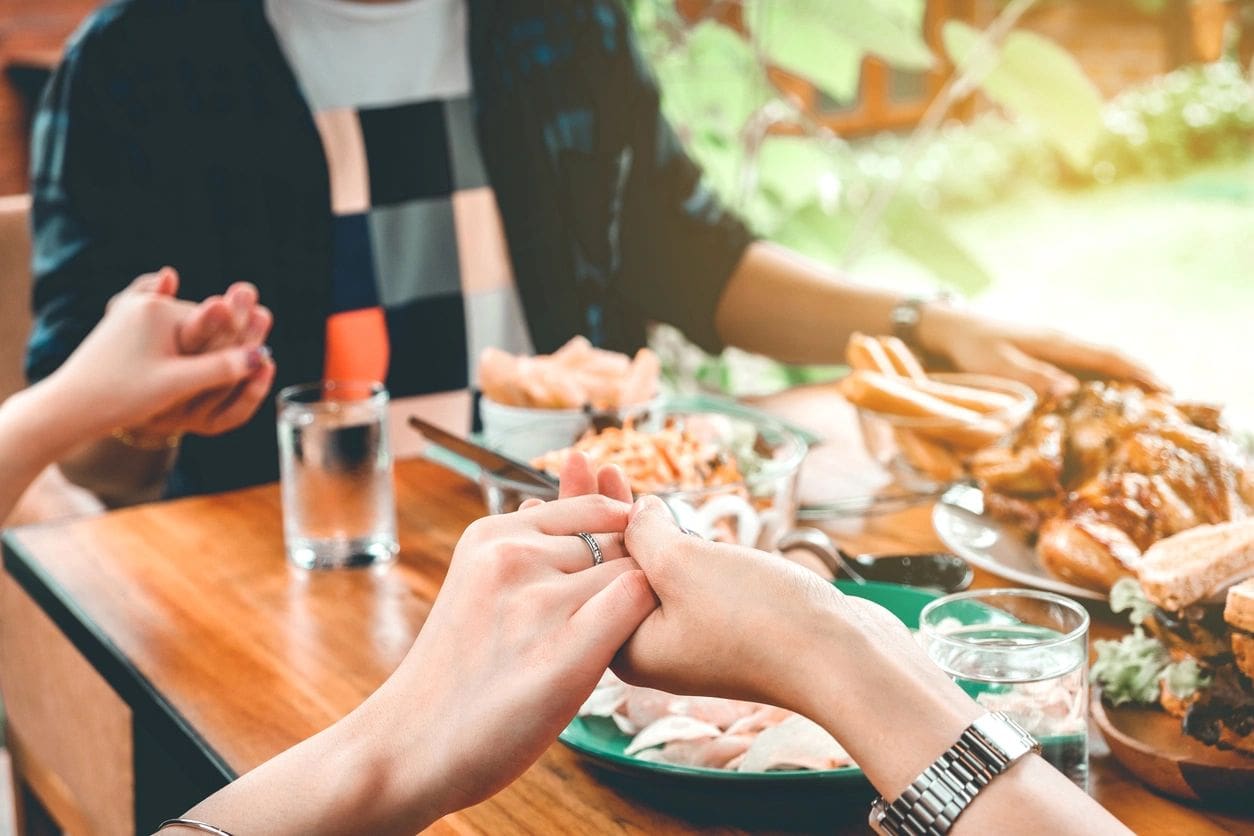 A group of people holding hands at a table with food.