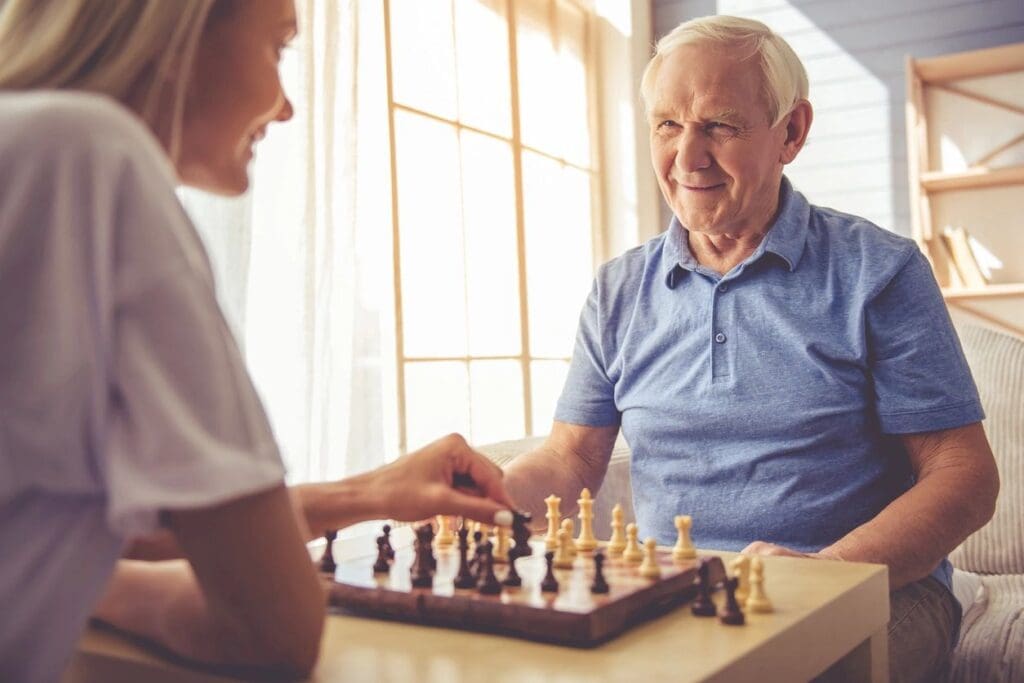 An elderly man and woman playing chess at home.