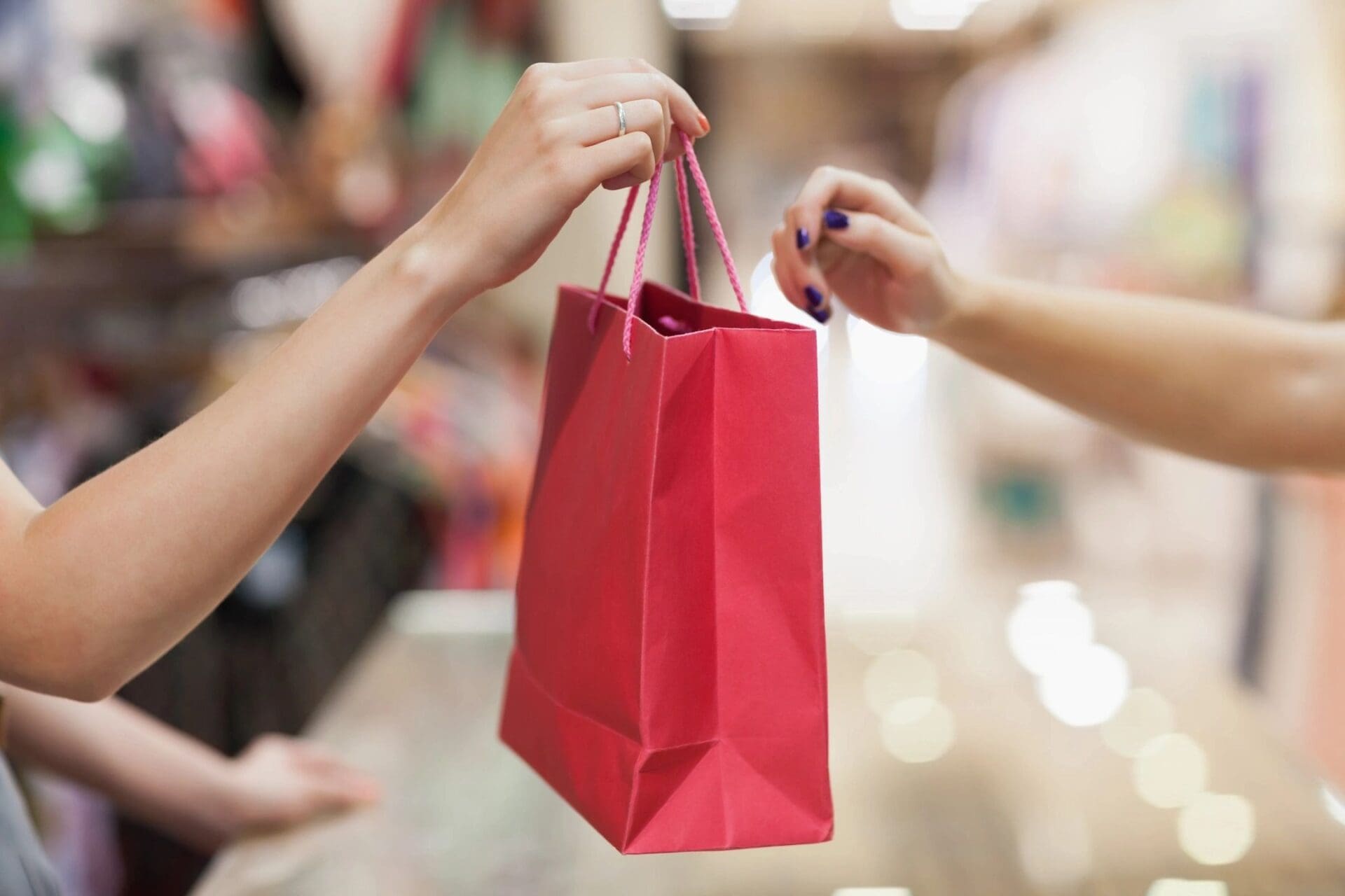 A woman handing a shopping bag to another woman in a store.