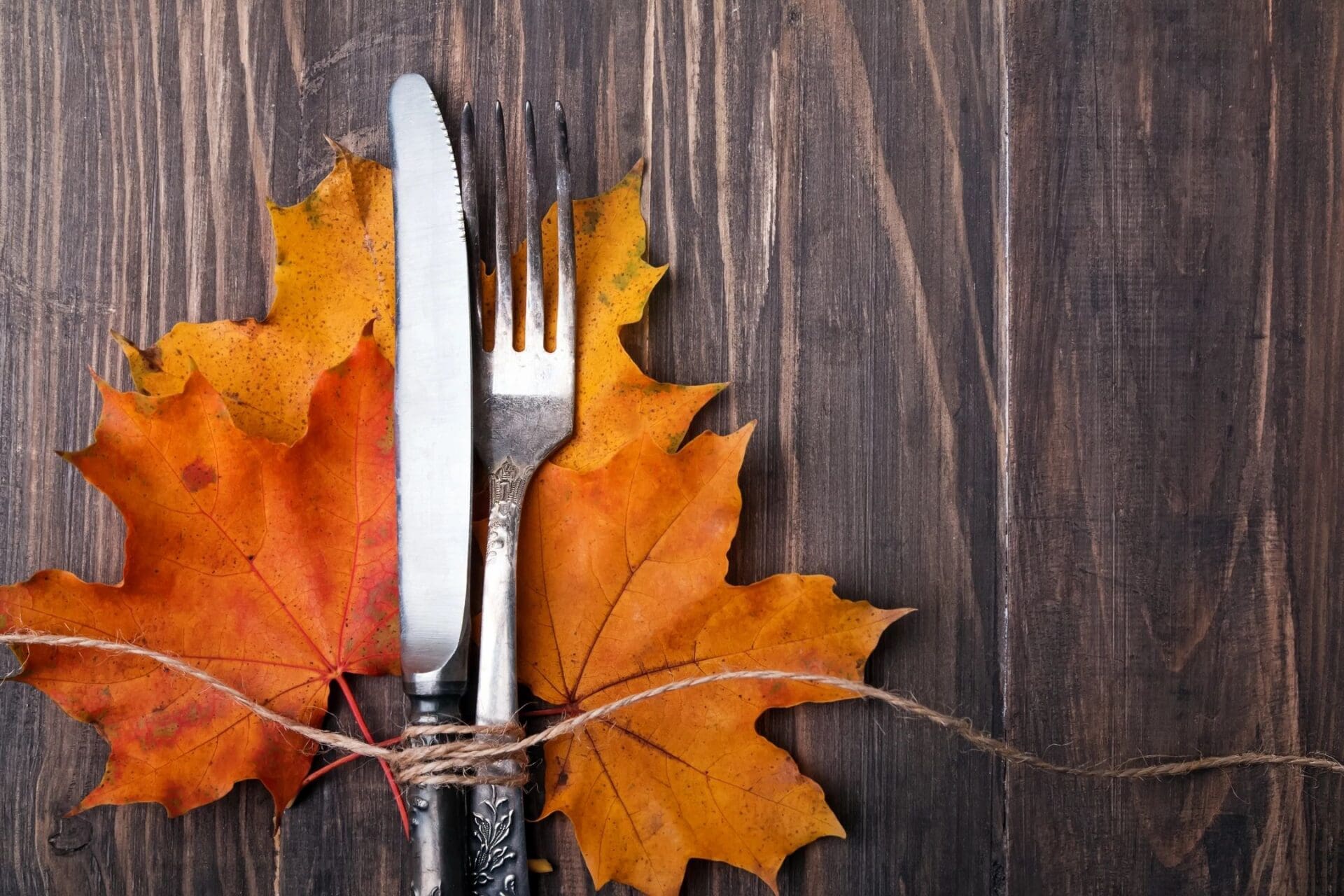 A fork, knife and autumn leaves on a wooden table.