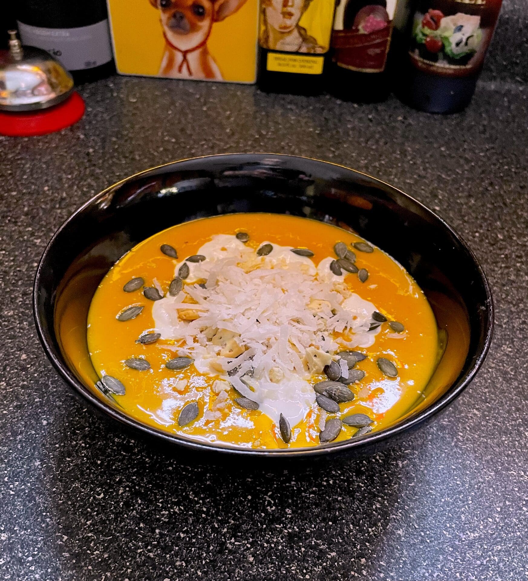 A bowl of soup with pumpkin seeds and parmesan cheese.