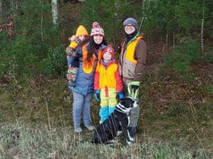 A family poses for a photo in a wooded area with a dog.