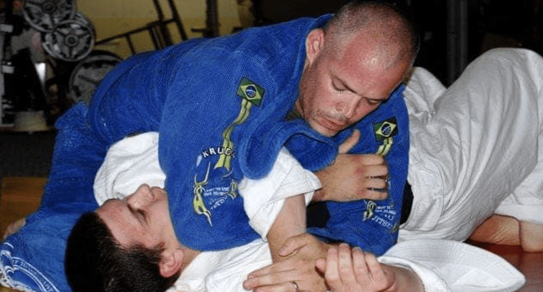 A man is doing a jiu jitsu choke on another man.