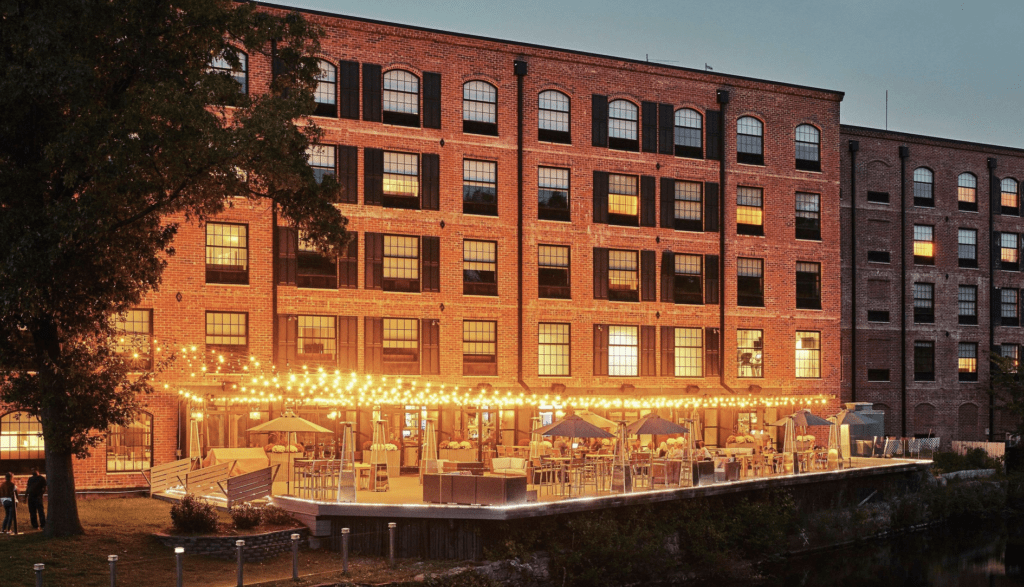 A brick building is lit up at dusk next to a river.