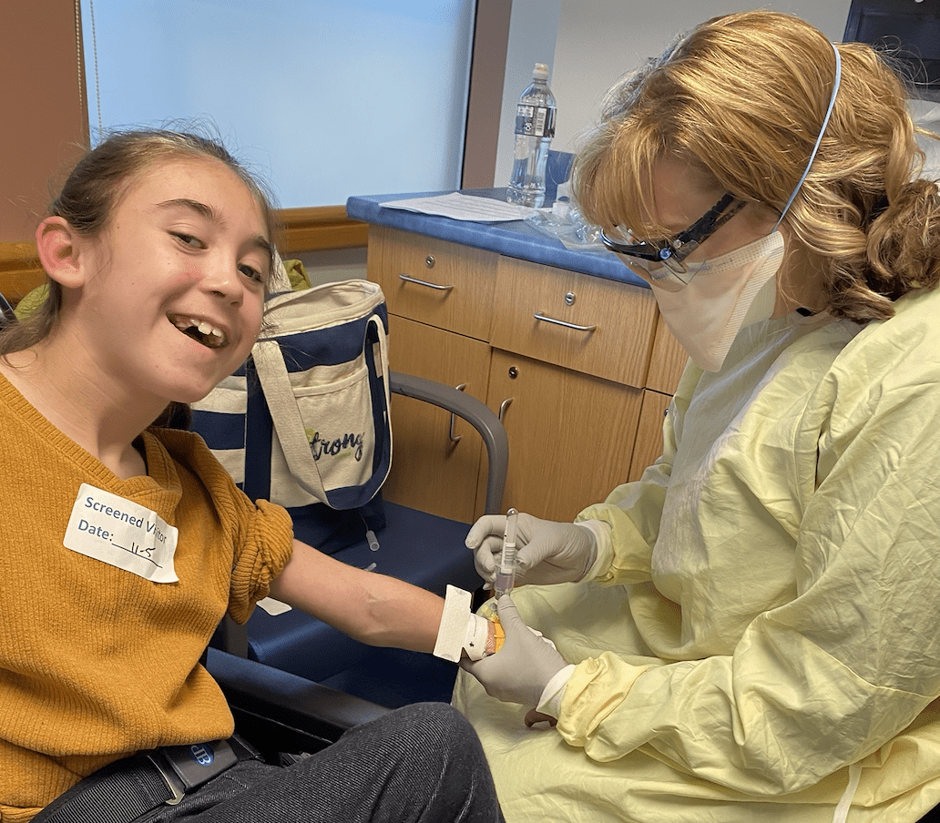 A young girl in a wheelchair getting her arm swabbed by a nurse.