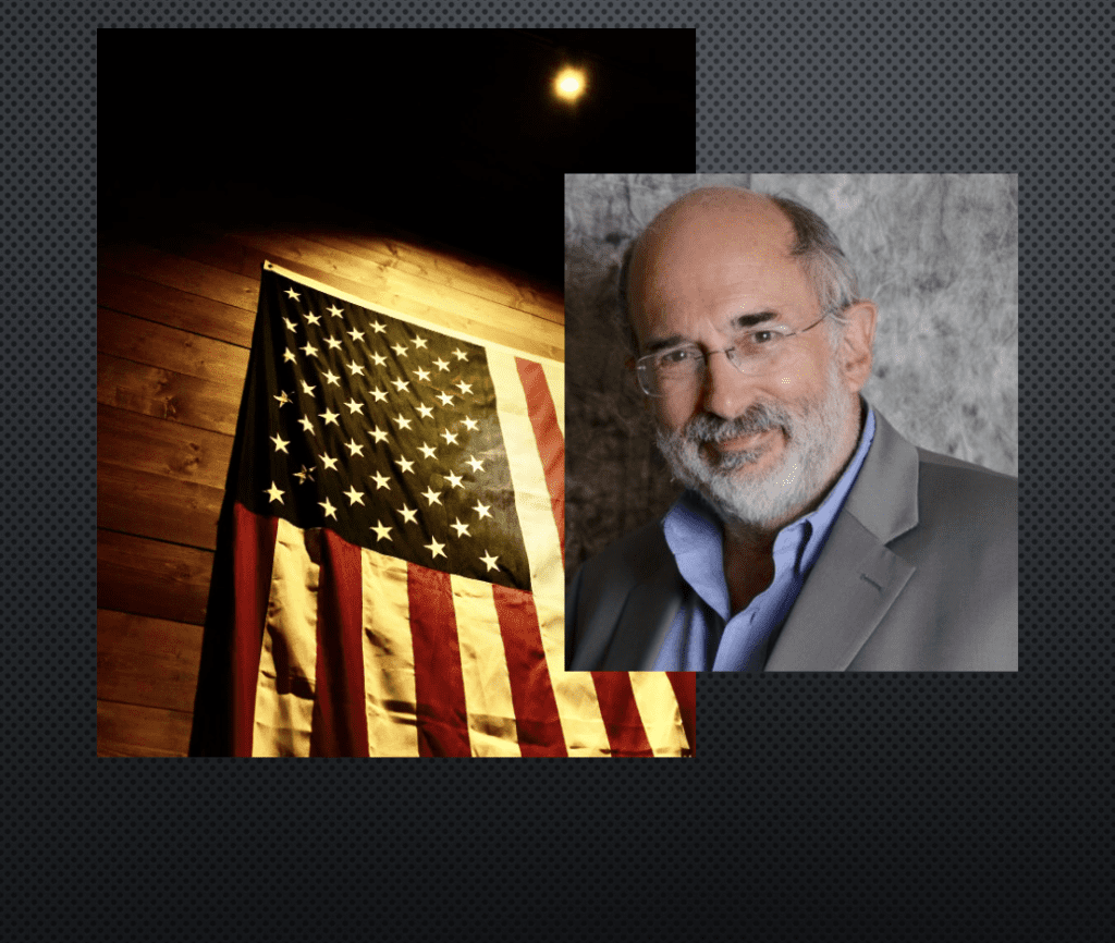 A man with a beard and glasses is standing next to an american flag.