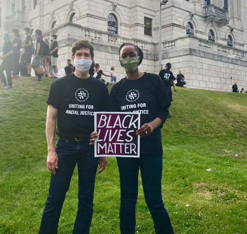 Two people holding a black lives matter sign in front of a building.