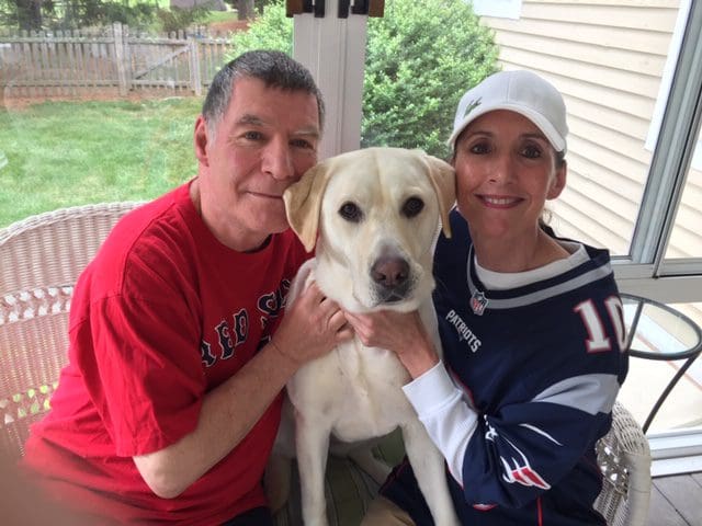 A man and woman posing with their dog on a porch.