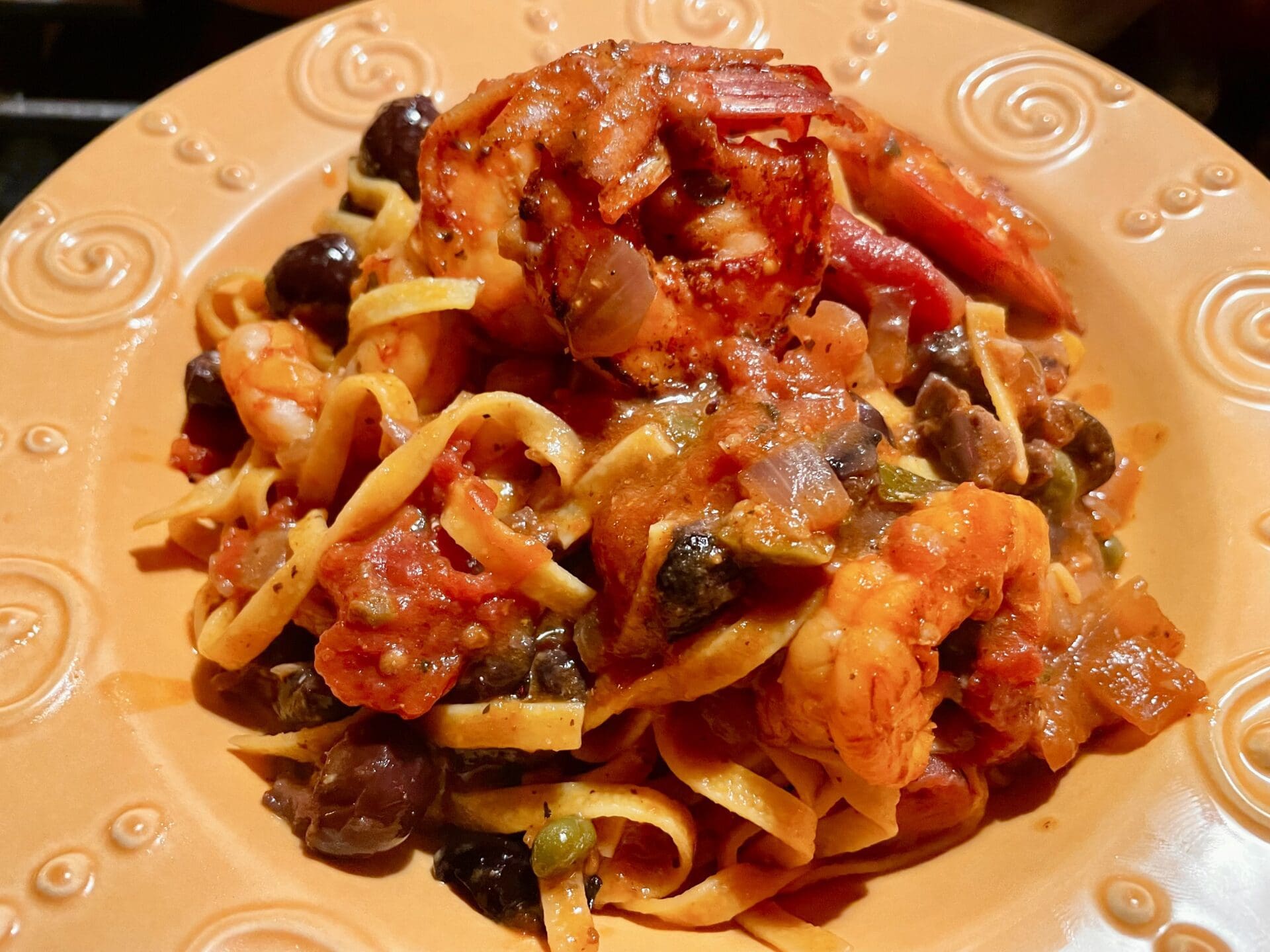 A plate of pasta with shrimp, olives and tomatoes.