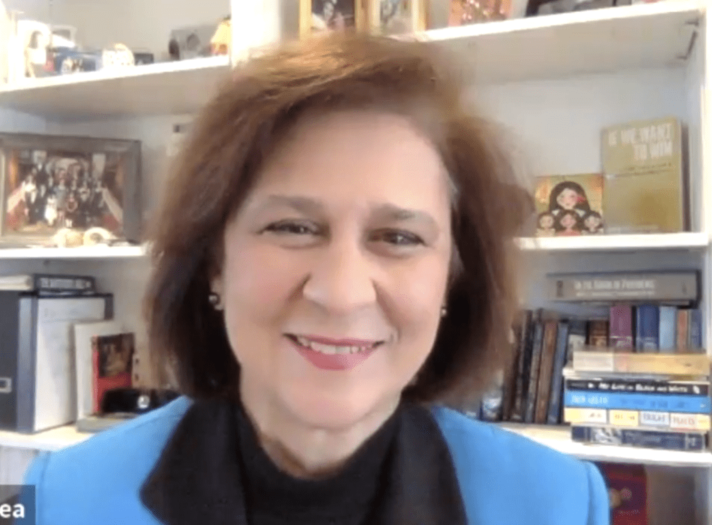 A woman in a blue jacket smiling in front of a bookshelf.