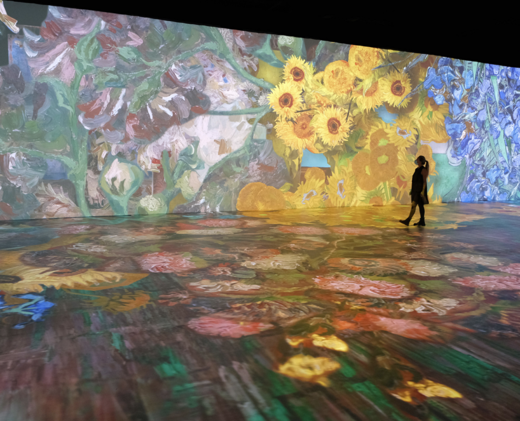 A woman is standing in front of a large projection of flowers.