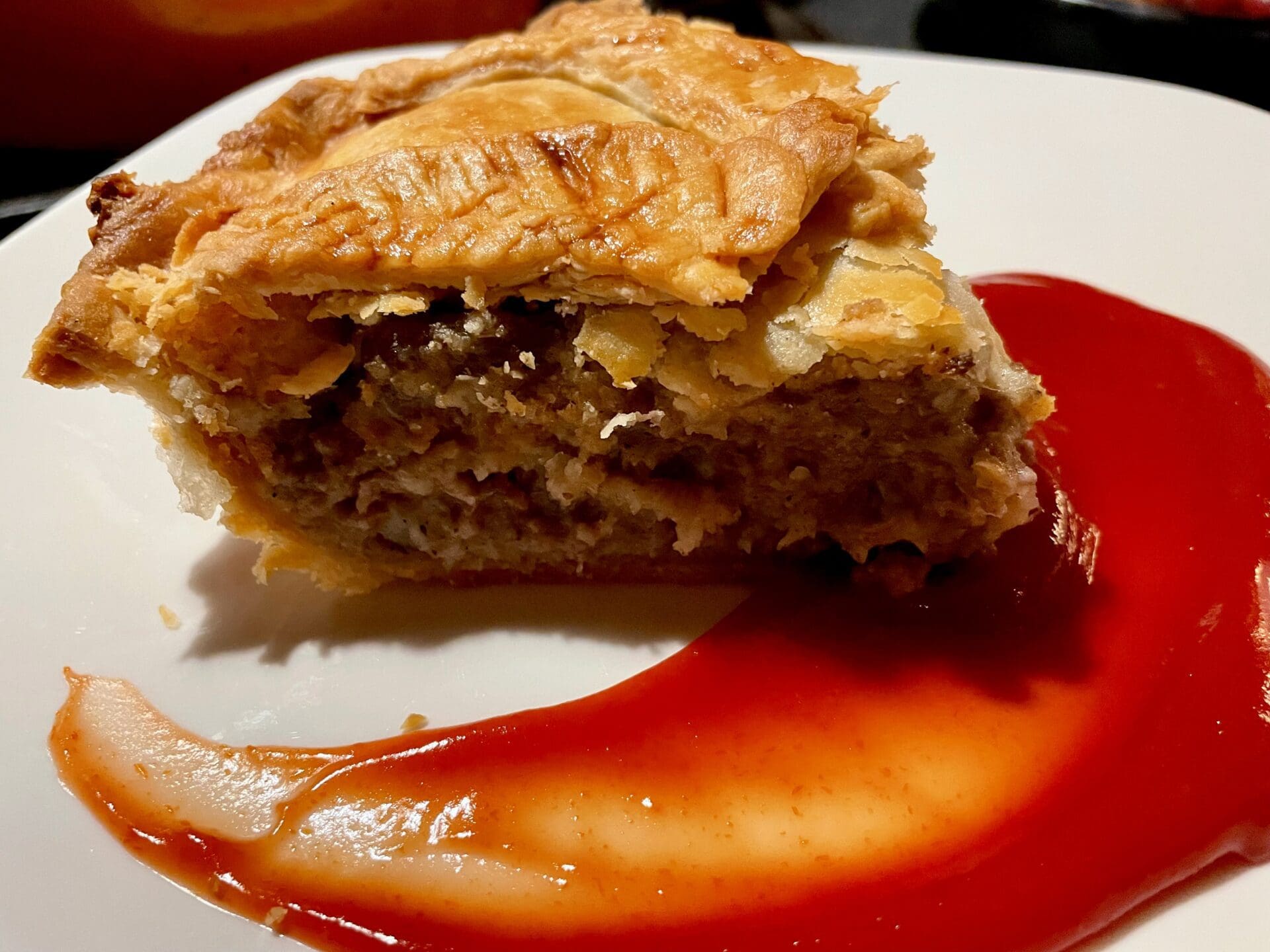 A piece of meat pie with sauce on a plate.