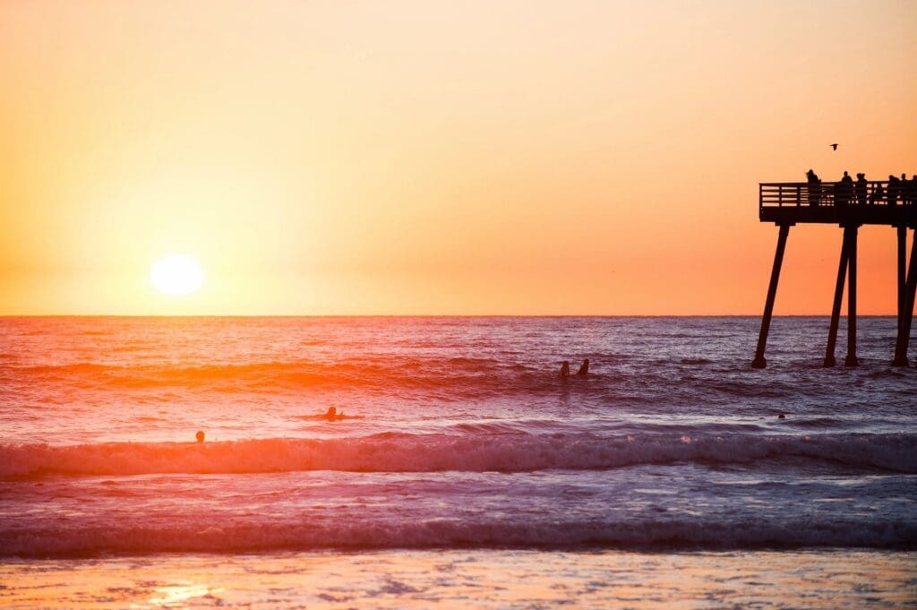 A group of surfers on a pier at sunset.