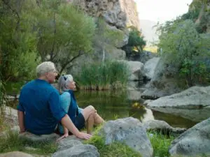 An older couple sitting on rocks near a pond.