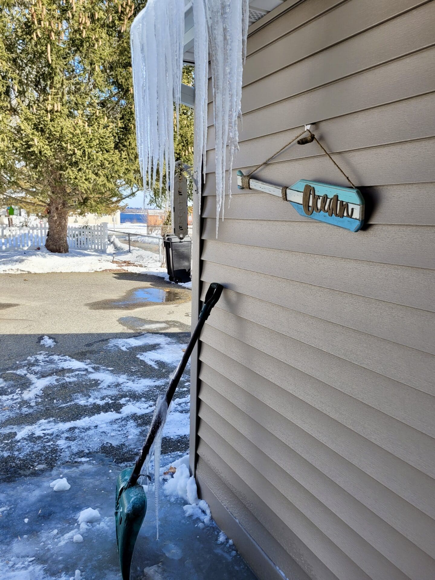 A shovel with icicles hanging from the side of a house.