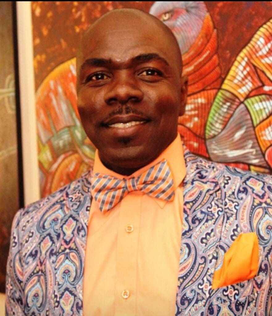 A black man in a blue suit and orange bow tie.