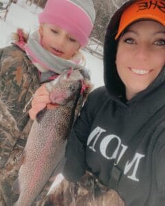 Two women holding up a rainbow trout in the snow.