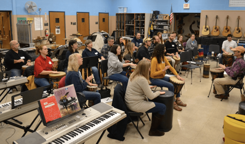 A group of people sitting in a classroom with music instruments.