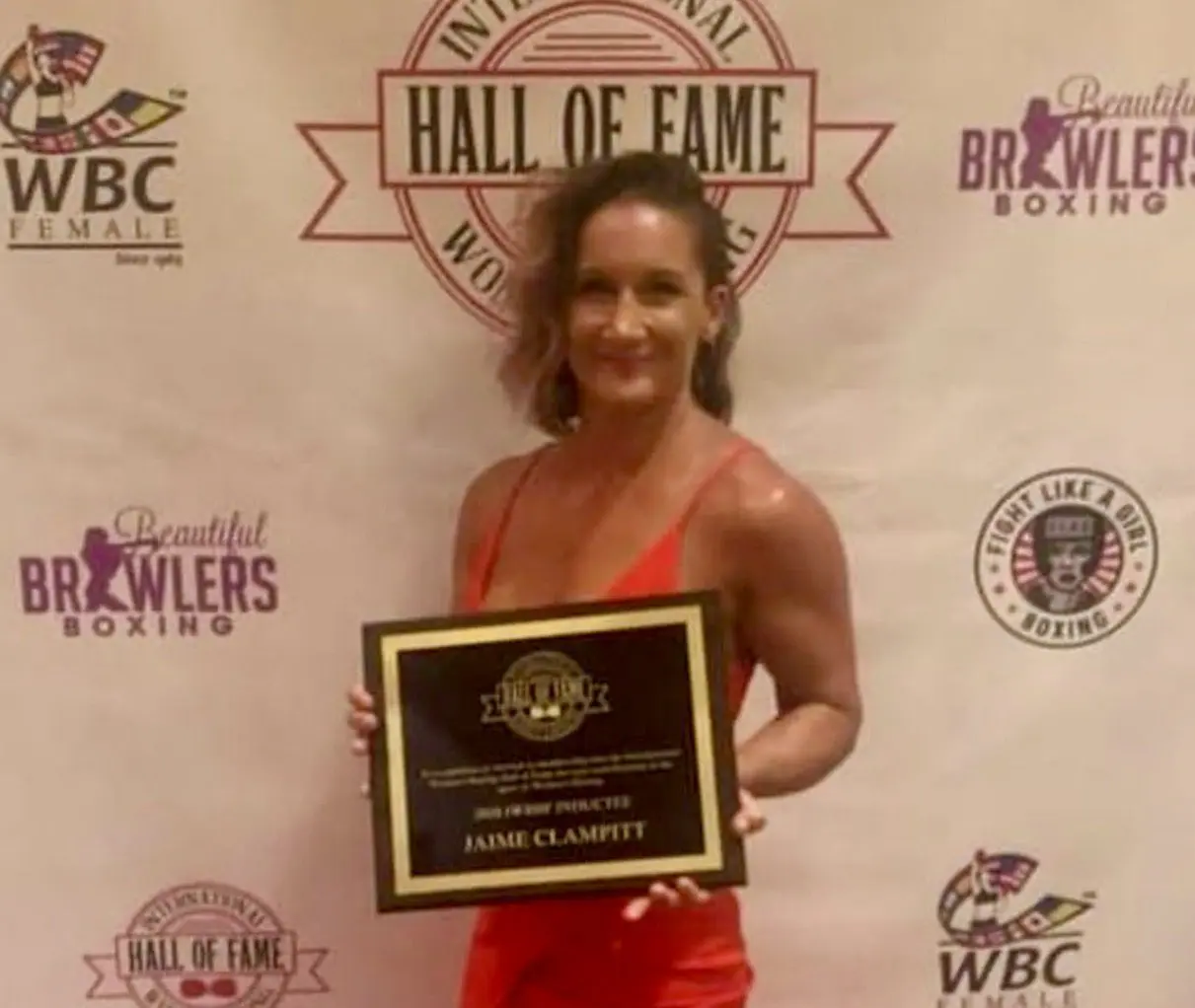 A woman in a red dress holding an award for the hall of fame.