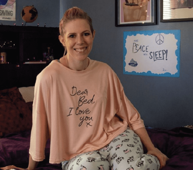 A woman in pajamas sitting on a bed with a sign.