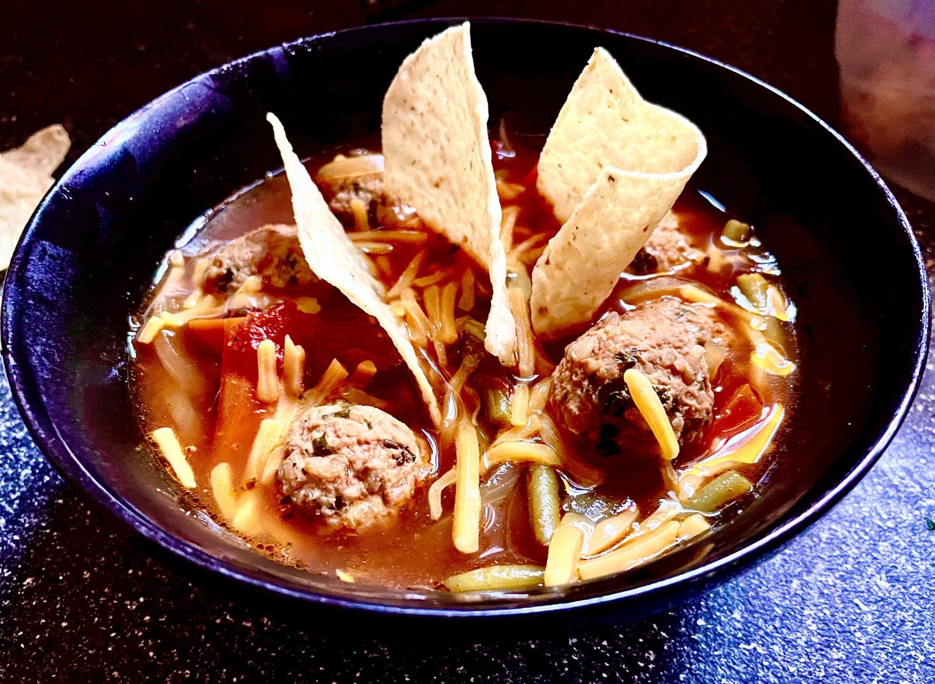 A bowl of soup with meatballs and tortillas.