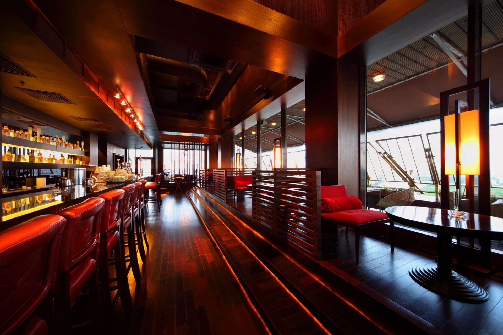 A bar with a wooden floor and red chairs.