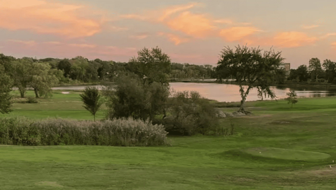 A golf course with trees and a lake at sunset.