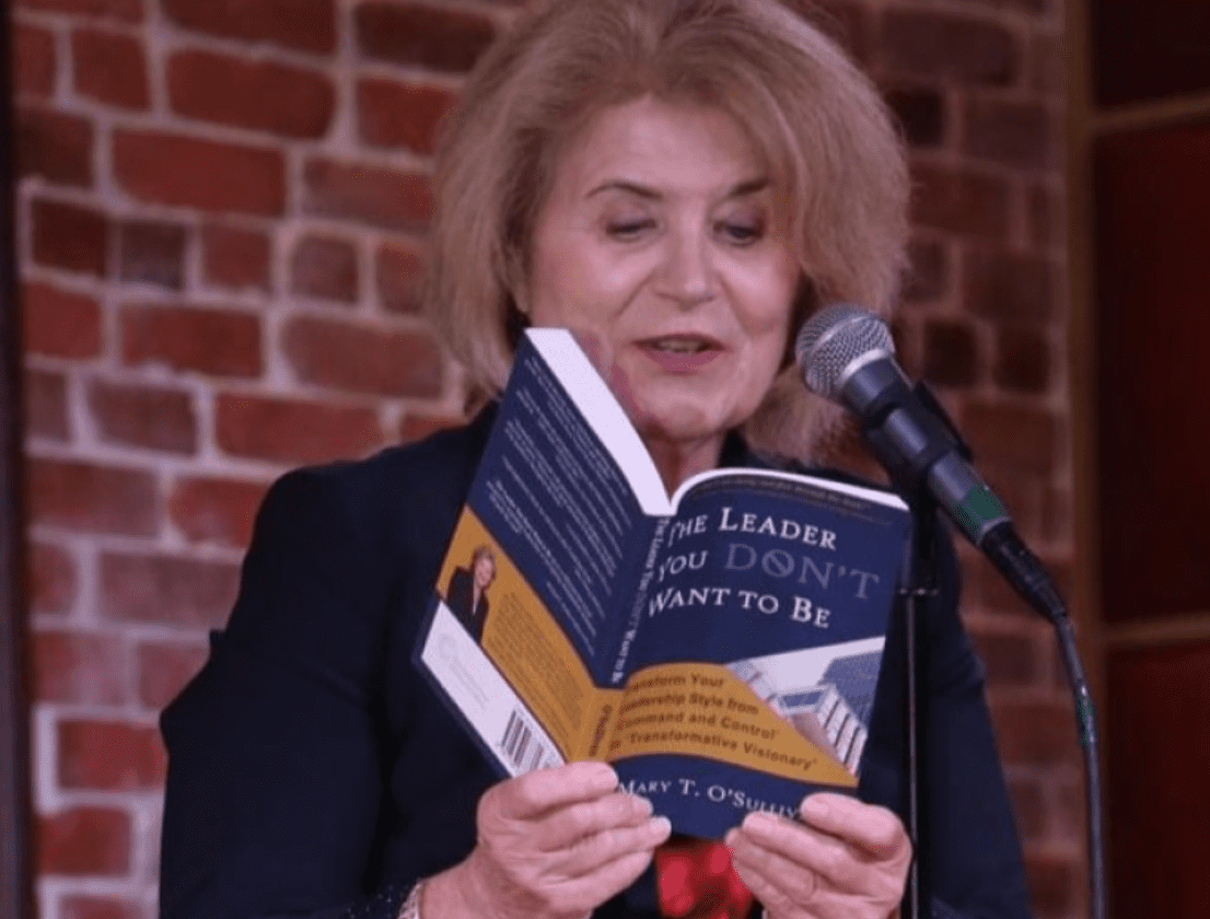 A woman reading a book into a microphone.