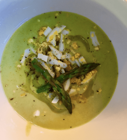 A bowl of green soup with asparagus and eggs.