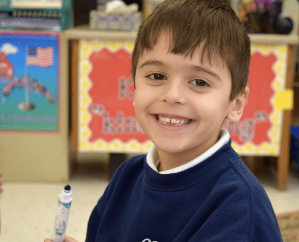 A young boy smiling while holding a pen.