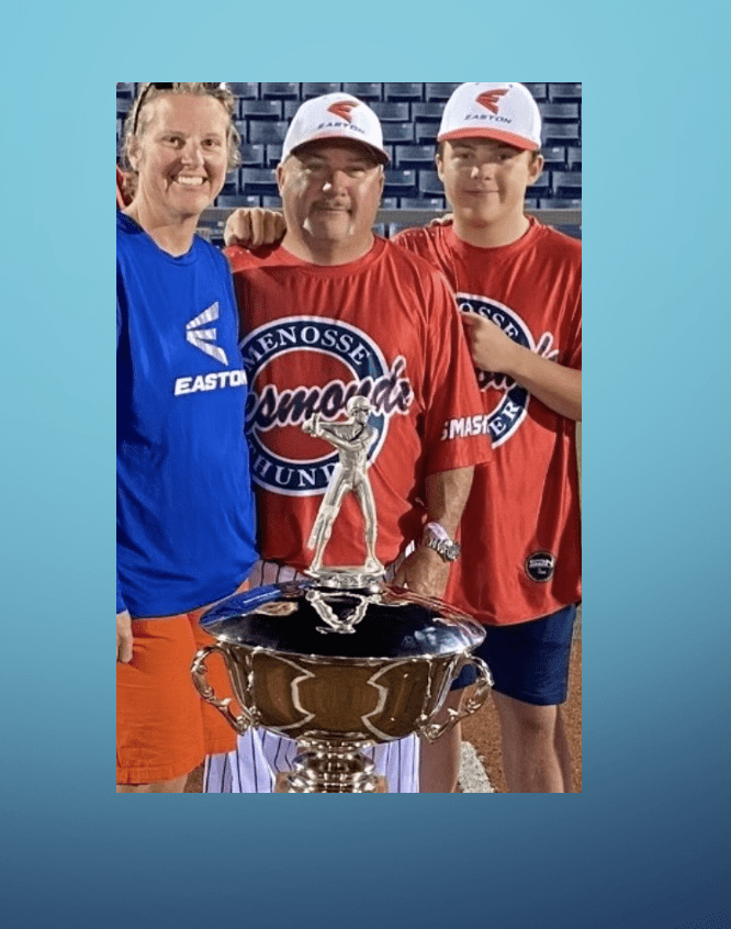 A family is posing with a trophy on a baseball field.