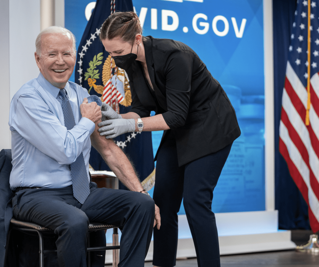 Joe biden getting a vaccine in front of an american flag.
