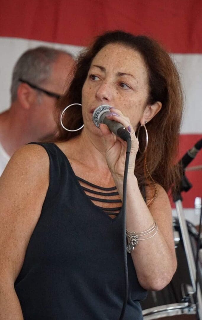 A woman singing into a microphone in front of an american flag.