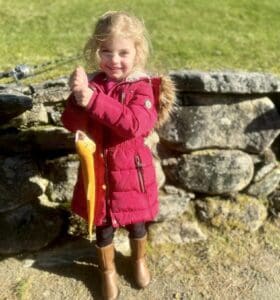 A little girl in a red coat standing next to a stone wall.