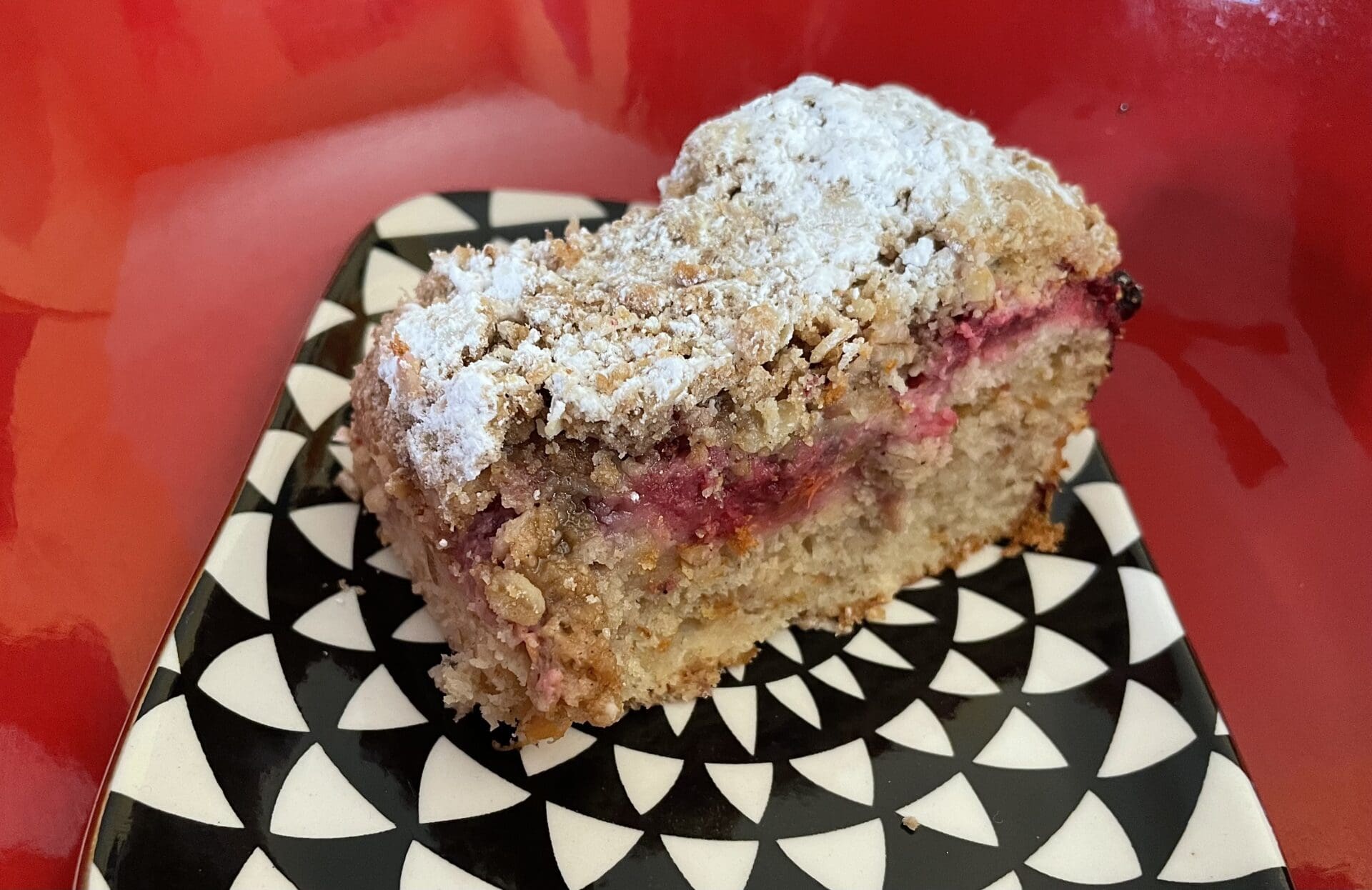A piece of raspberry coffee cake on a black and white plate.
