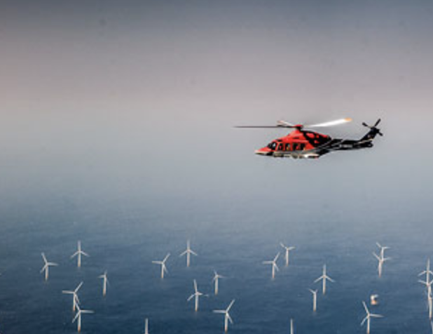 A helicopter flying over wind turbines.