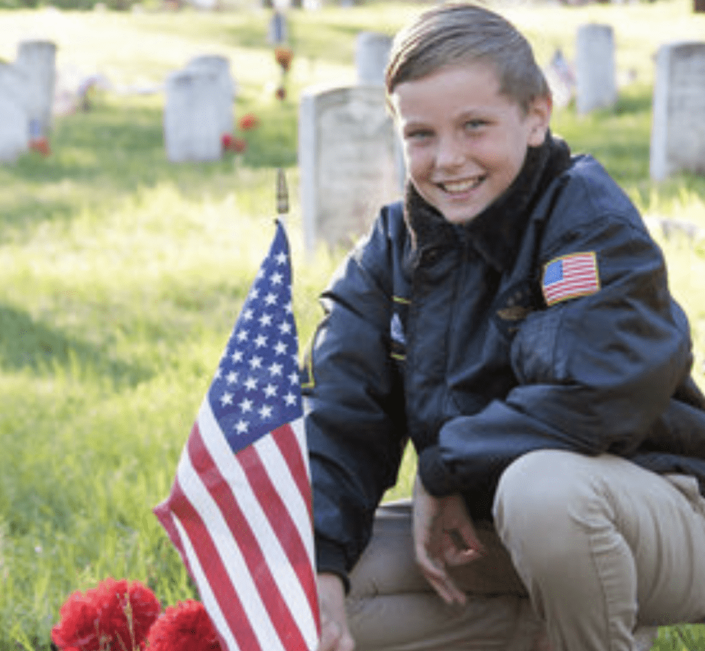 A boy kneeling in front of a grave with an american flag.