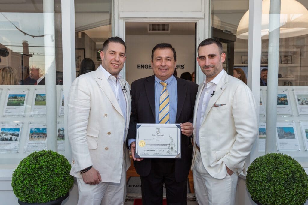 Three men in suits holding a certificate in front of a store.
