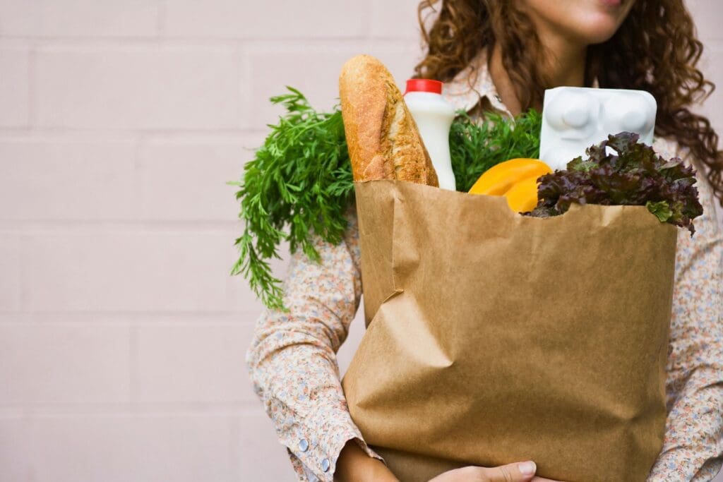 A woman holding a shopping bag full of groceries.