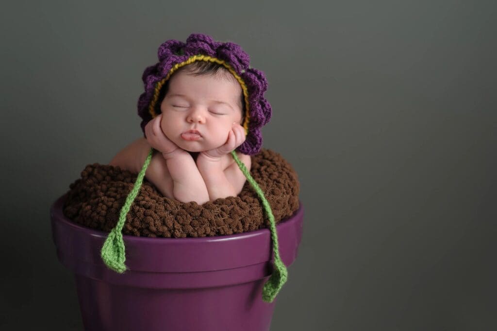 A baby sleeping in a purple pot with a knitted hat.