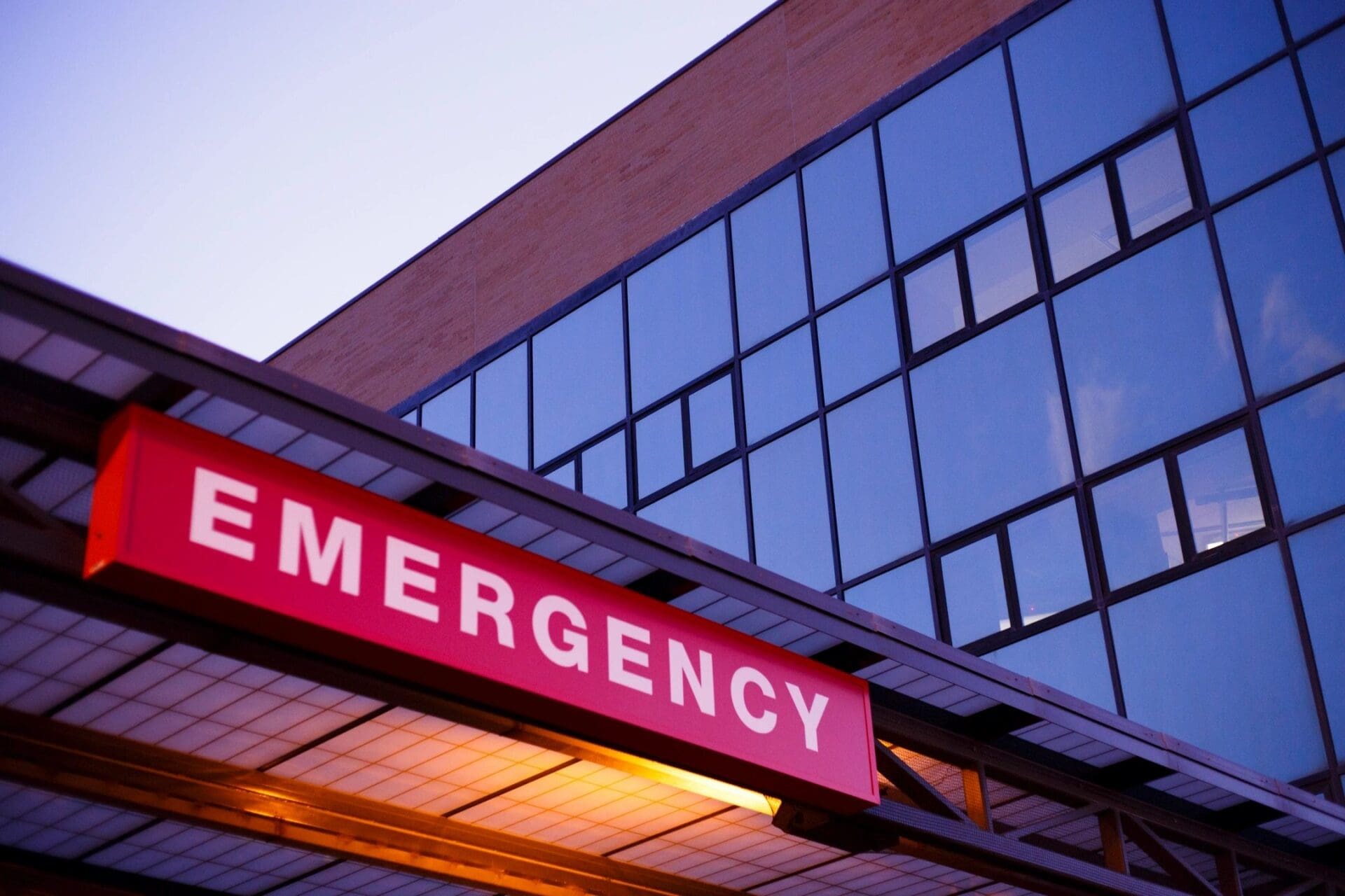 A hospital emergency sign is lit up at dusk.