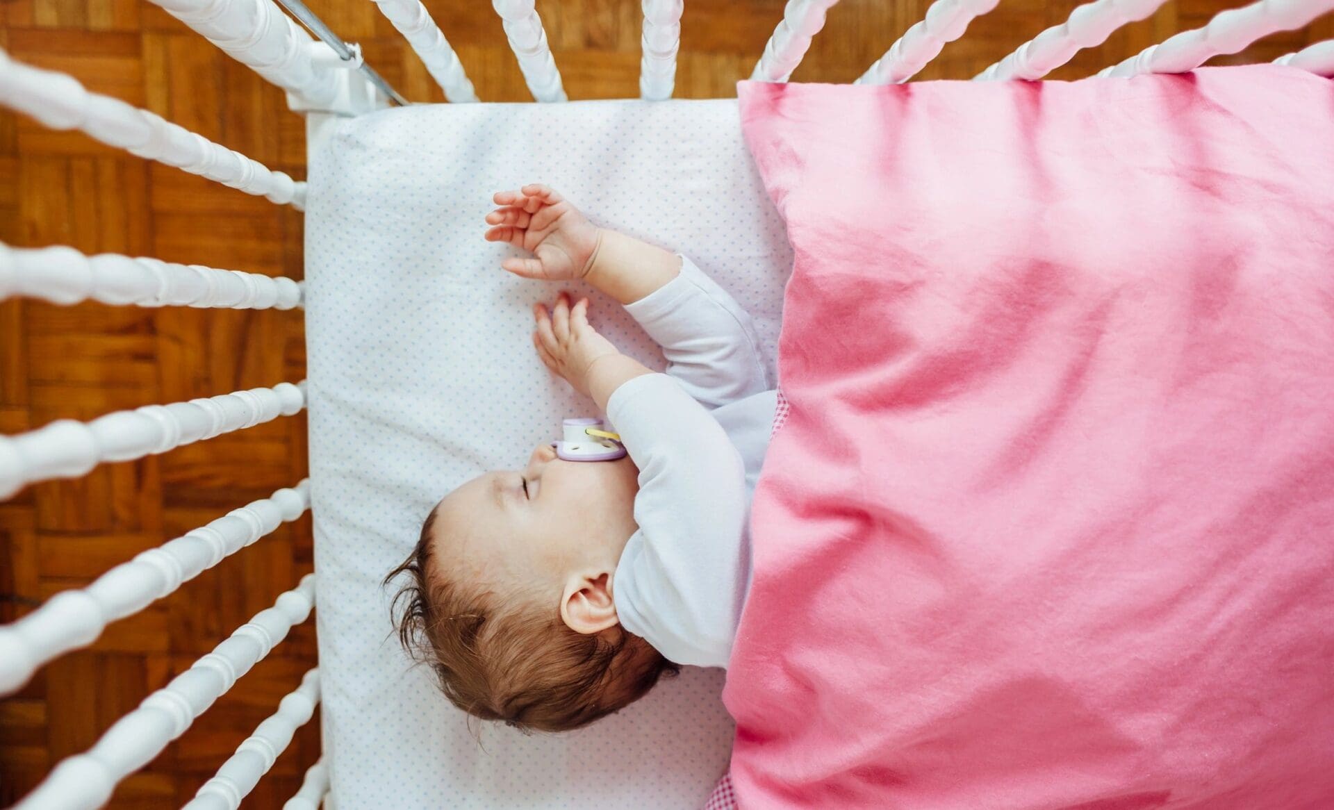 A baby sleeping in a crib with a pink blanket.