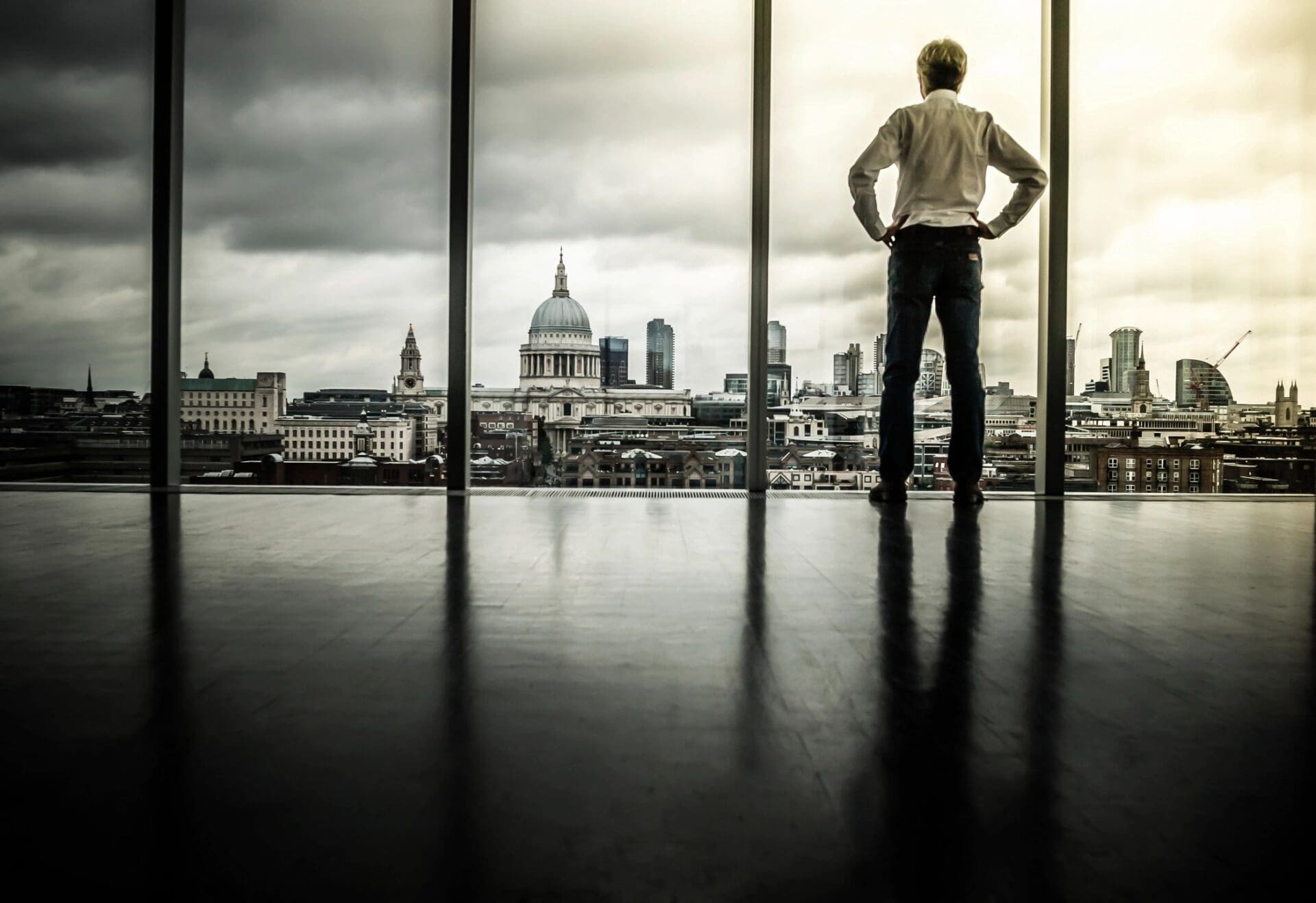 A businessman looking out of a window at london's skyline.