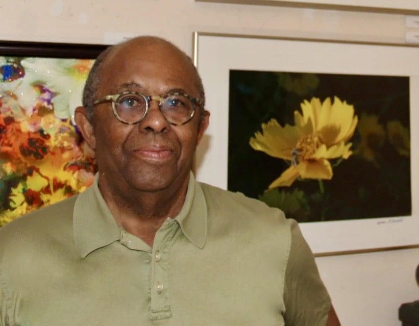 A man in glasses standing in front of a yellow flower.