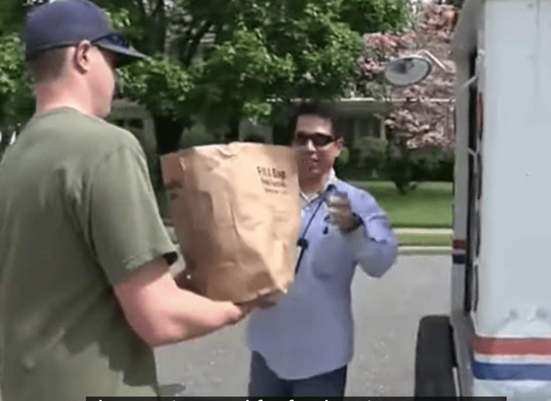 A man is handing a bag to a man in front of a delivery truck.